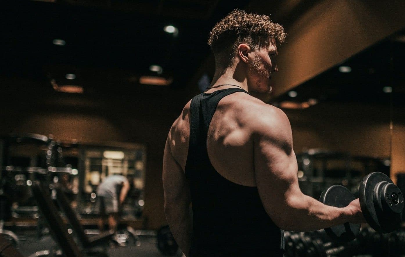 An athlete doing a dumbbell curl in a dim gym