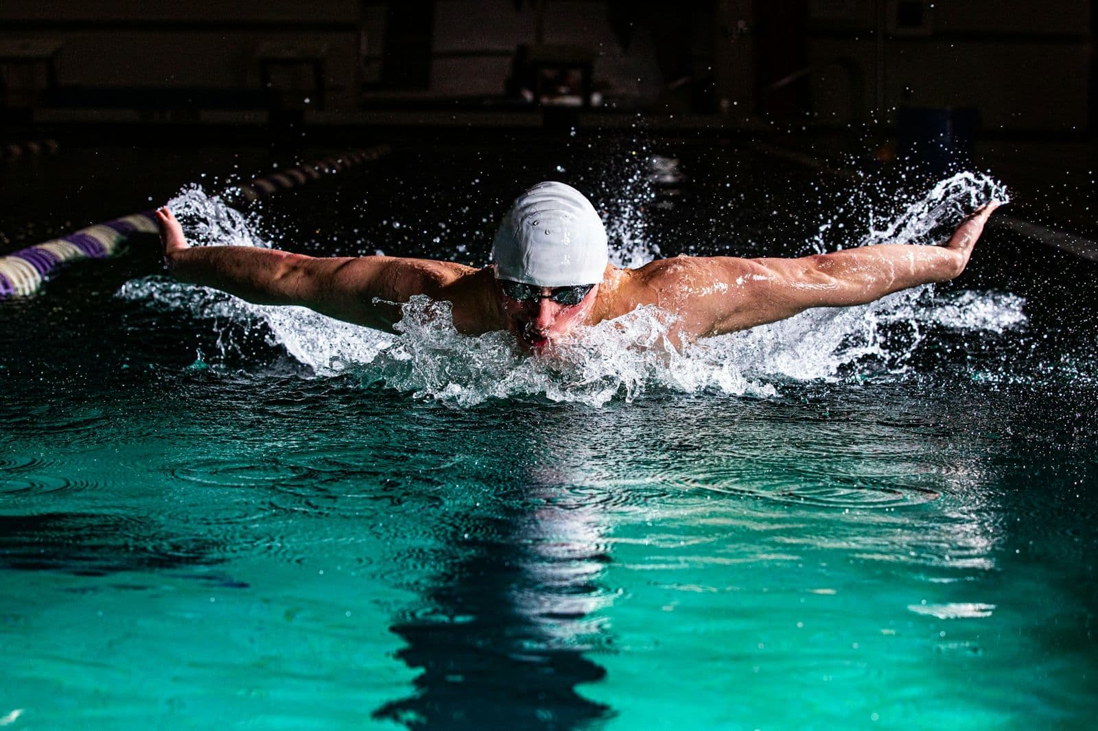 A swimmer doing butterfly in a dark indoor pool